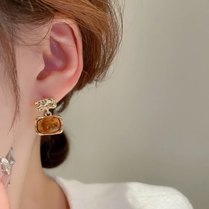 Close-up of geometric resin drop earrings in amber with textured golden metal finish