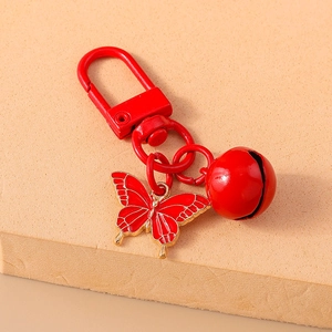 Detail of red enamel butterfly keychain with gold edges and small metal bell pendant
