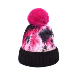 Tie-dye cable knit winter beanie for women with bright pink faux fur pompom and black cuff
