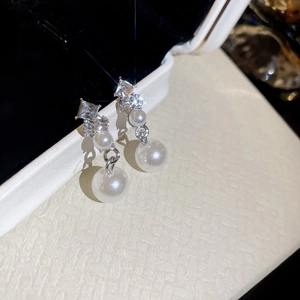 Detailed close-up of diamond-encrusted silver earrings with elegant white pearls in a box