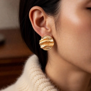 Close-up of 18k gold-plated hammered round stud earrings worn by a model in warm light