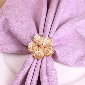 Detail of matte gold flower napkin ring on purple fabric and white ceramic plate