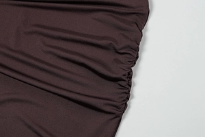 Close-up of the ruching detail on a chocolate brown knit dress with side pleats