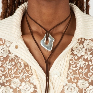 Detail view of irregular silver liquid pendant on brown cord necklace worn by model