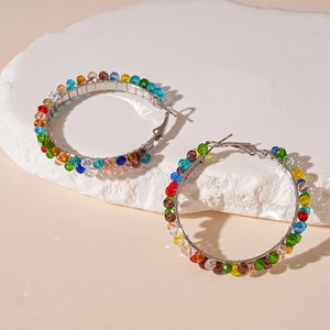 Detailed macro shot of colorful glass beads on silver hoop earrings over textured stone