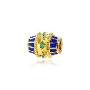 Macro detail of gold-plated oval bead with blue enamel stripes and green zircon inlay