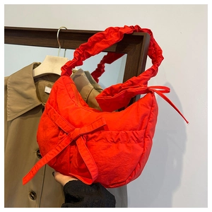 Detail of red crescent shoulder bag featuring ruched handle and large bow decoration