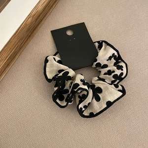 Chic black and white floral fabric scrunchie with hemmed edges on a neutral background