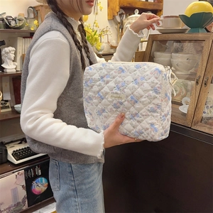 Trousse à maquillage matelassée avec motifs d'oursons et nœuds bleus portée à la main