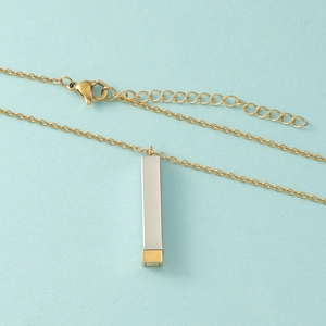 Collier rectangulaire argent et doré avec fermoir mousqueton sur fond bleu ciel