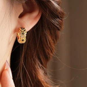 Close-up of vintage gold hoop earring with green gems and zircons worn by a model
