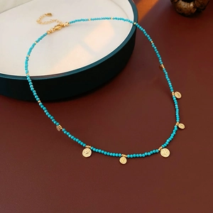 Détail du collier de perles turquoise avec pendentifs ronds dorés sur plateau bleu