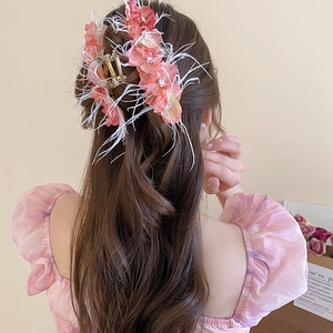 Détail d'une pince à cheveux avec fleur en dentelle rose, plumes blanches et strass