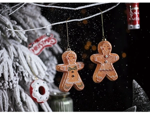 Detailed view of gingerbread man ornaments hanging on snowy Christmas tree branches