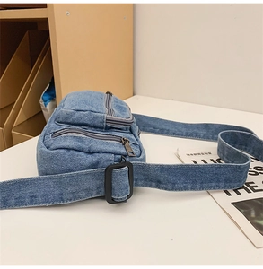 Detail view of washed denim crossbody bag featuring multiple zipper pockets and adjustable strap