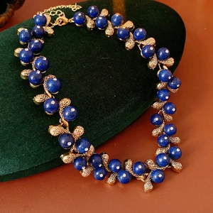Detail of blue beaded vintage necklace with gold leaf accents on a green velvet pad