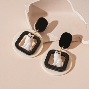 Cute black and white acrylic cat drop earrings with gold hooks on a beige stone stand