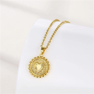 Detail of gold necklace with a round beaded pendant featuring an engraved heart center