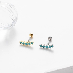 Close-up of gold and silver screw-back cartilage earrings with turquoise gemstones