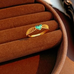 Vue macro d'une bague ouverte dorée avec pierre verte en cœur sur du velours