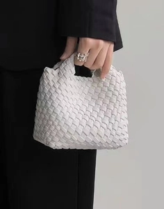 Detailed shot of a white woven bucket bag held by a model in a black suit