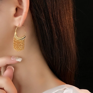 Close-up of elegant gold C-shaped earrings with hanging tassel chains on model