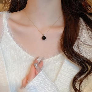 Close-up of elegant gold chain necklace with a black pearl pendant and sparkling zircon