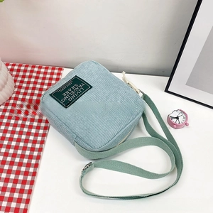 Macro detail of a light blue corduroy crossbody bag with a green fabric logo patch