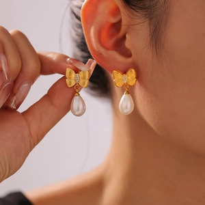 Elegant gold bow earrings with crystal accents and white drop pearls worn by a model