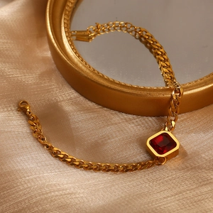 Nahaufnahme des goldenen Panzerarmbands mit rotem Zirkonia auf champagnerfarbenem Satin
