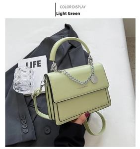Close-up of light green crossbody bag with silver chain detail and fashion text
