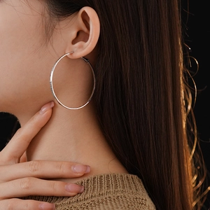 Close-up of silver-toned textured hoop earrings worn by a model in soft lighting