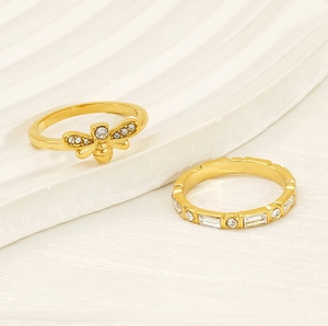 Macro shot of gold bee ring and rectangular crystal eternity band on white waves