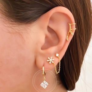Macro shot of gold hoop earrings with square purple zircon pendant and floral stud ear cuff