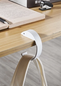 Portable white desk hook holder securely holding a canvas bag on a wooden table edge