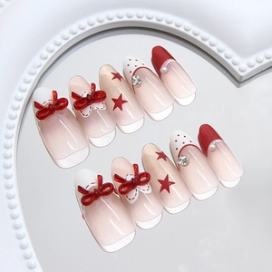 Red bow and polka dot press-on nails with stars and rhinestone accents in almond shape