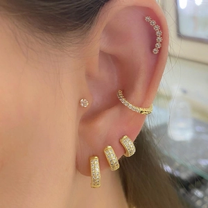 Close-up of golden C-shaped earrings and ear cuffs with pavé white zircon on a model