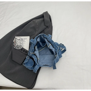 Detailed top view of blue denim tote bag with zipper and decorative cards on white fabric