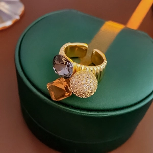 Detail of gold-plated ring with grey stone, orange crystal and pavé zircon ball