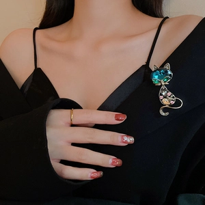 Detail view of a cat brooch with a blue heart gemstone and colorful crystals on a black coat
