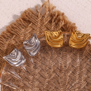Detail of square wavy textured gold and silver earrings on a glass plate tray