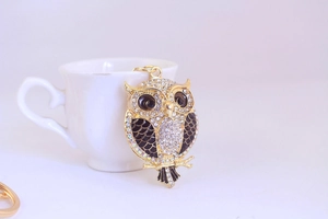 Detailed view of a golden metal owl keychain featuring sparkling rhinestones and black enamel