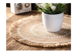 Detailed close-up of handmade jute placemat with white patterns and tassels on a wooden table