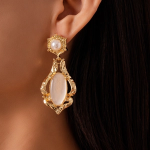 Macro view of vintage gold earrings with pearl and oval iridescent stone on a model