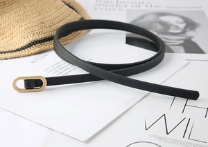 Close-up of a slim black belt featuring a polished gold oval buckle on a stylist background