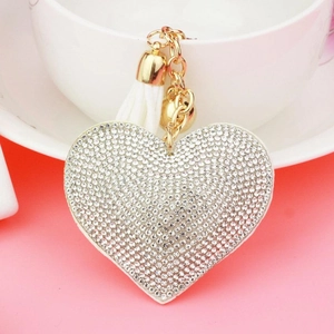 Detail of heart-shaped leather keychain with rhinestones, golden bell and white tassel