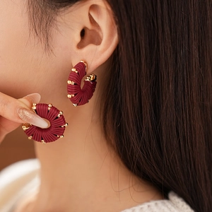 Macro detail of wine red woven leather earrings with decorative golden metal beads