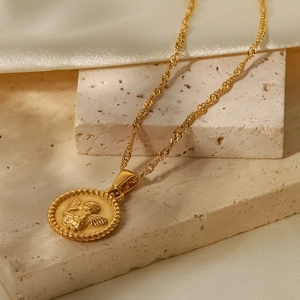 Close-up of vintage gold angel relief pendant on a twisted chain over white silk