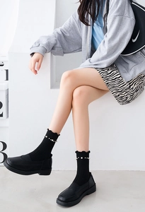 Detail of black crew socks featuring elegant ruffle cuffs and decorative white pearls