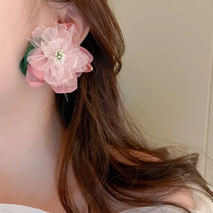 Close-up of elegant pink lace flower earrings with green leaf details on model's ear